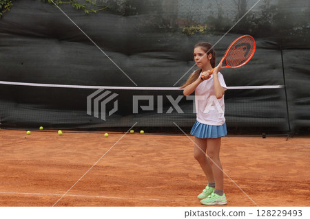 Young girl practicing tennis on a red clay court 128229493