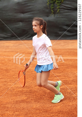 Young girl playing tennis on a clay court during practice 128229507