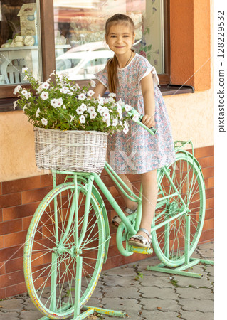 Girl posing with a decorative bicycle featuring a flower basket in springtime 128229532