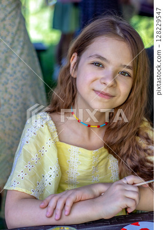 Young girl in a yellow dress engaging in creative outdoor painting activity Young girl in a yellow dress engaging in creative outdoor painting activity 128229547