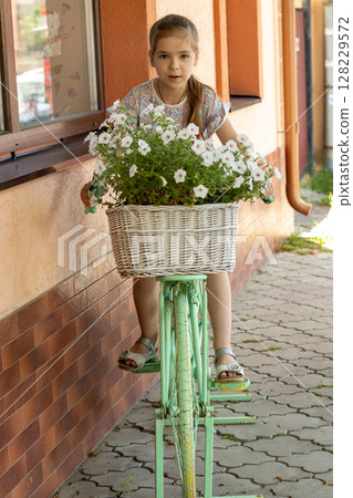 Young girl riding decorative bicycle with flowers in a basket outdoors 128229572