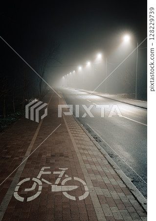 Empty Bicycle Lane in Foggy Night Street Illuminated by Streetlights Empty Bicycle Lane in Foggy Night Street Illuminated by Streetlights 128229739