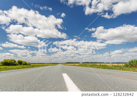 Endless asphalt road stretching through a summer landscape of green fields under a sunny sky Endless asphalt road stretching through a summer landscape of green fields under a sunny sky 128232642