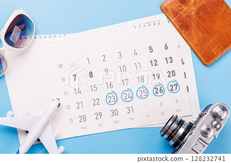 Travel-themed flat lay with calendar, toy airplane, camera, and sunglasses 128232741