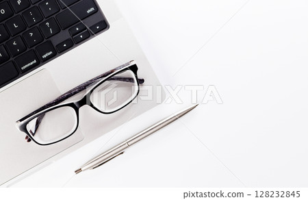 Closeup of an office table featuring a sleek laptop and reading glasses on a clean white surface Closeup of an office table featuring a sleek laptop and reading glasses on a clean white surface 128232845