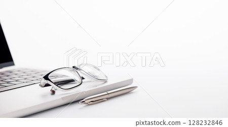 Closeup of an office table featuring a sleek laptop and reading glasses on a clean white surface Closeup of an office table featuring a sleek laptop and reading glasses on a clean white surface 128232846