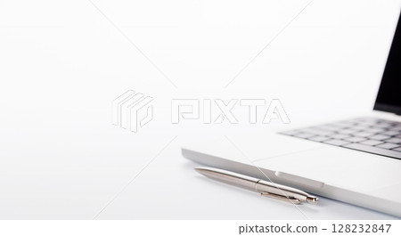 Closeup of an office table featuring a sleek laptop, a pen, and pencil on a clean white surface 128232847