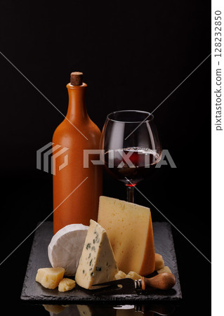 A refined selection of aged cheeses presented on a board, accompanied by a glass of wine 128232850