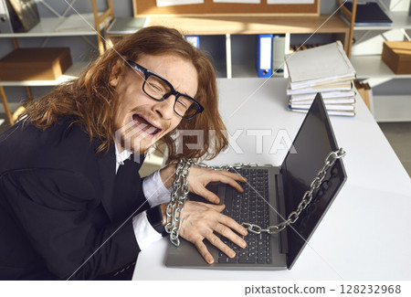 Tired office worker sitting at desk chained to laptop and crying unable to go home 128232968