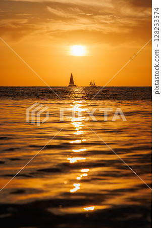 Sunset over the sea with sailing boats on the horizon Sunset over the sea with sailing boats on the horizon 128233574