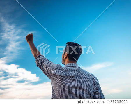 A man holding a pen high in his hand under the blue sky 128233651