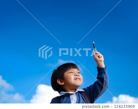A child raising a pen in his hand under the blue sky 128233909