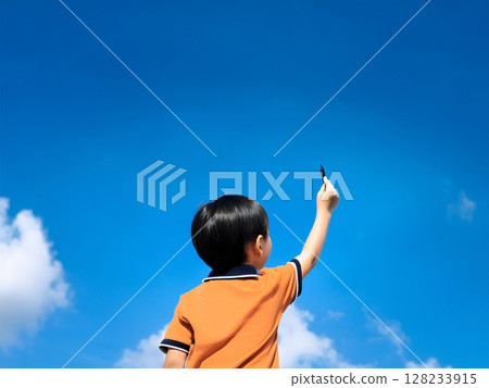A child raising a pen in his hand under the blue sky 128233915