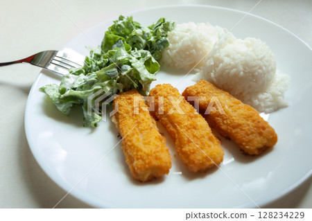 A dish of fish fingers, rice and salad with cream on a plate A dish of fish fingers, rice and salad with cream on a plate 128234229