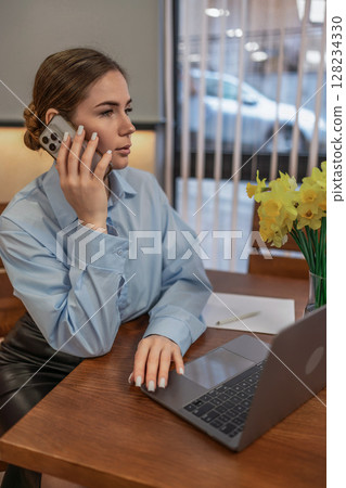 Woman Phone Laptop, indoor daytime work: Lady talks on phone, by laptop at desk, maybe solving issue. 128234330