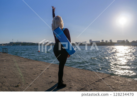 Yoga Woman Beach Sunrise Pose - Woman practicing yoga on a beach with a yoga mat at sunrise. Yoga Woman Beach Sunrise Pose - Woman practicing yoga on a beach with a yoga mat at sunrise. 128234470