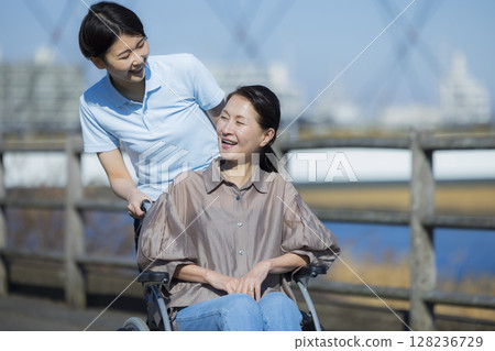 A female caregiver pushing a woman in a wheelchair 128236729