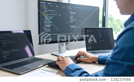 The hands of a male engineer operating a keyboard. An image of programming on multiple monitors. 128237098