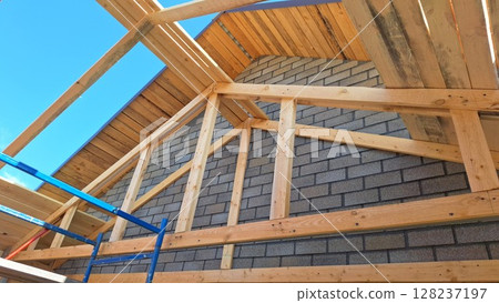 Wooden roof trusses and brick wall under construction against blue sky 128237197