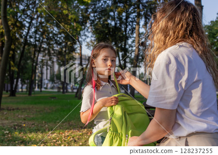 Morning routine in park: parent prepares child for school with backpack 128237255