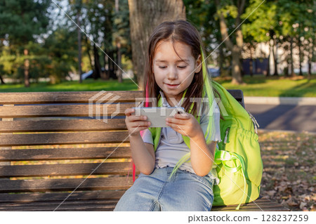 Young girl playing on smartphone outdoors in park on sunny day Young girl playing on smartphone outdoors in park on sunny day 128237259