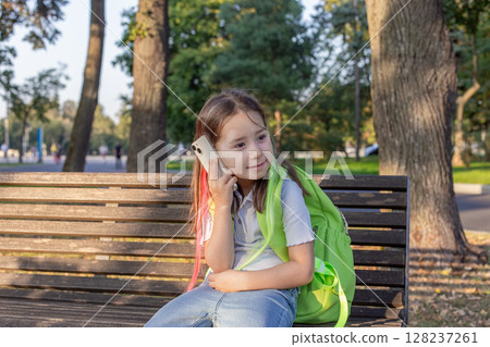 Young girl with backpack using smartphone on park bench Young girl with backpack using smartphone on park bench 128237261