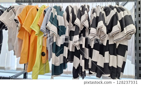 Colorful and striped t-shirts hanging on rack in sunlit room 128237331