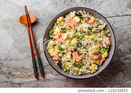 Asian food fried rice with salmon, seaweed, green peas, onion and egg close-up in bowl. Horizontal top view 128238855