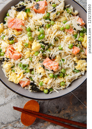 Asian fried rice with red fish, seaweed, green peas, onion and omelet close-up in a bowl on the table. Vertical top view 128238860