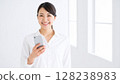 A smiling woman holding a smartphone in her hand. A clean and bright image. 128238983