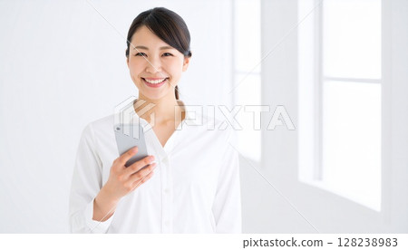 A smiling woman holding a smartphone in her hand. A clean and bright image. 128238983