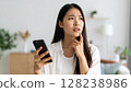 An image of a woman holding a smartphone in her hand and looking worried or in distress. 128238986