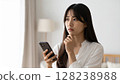 An image of a woman holding a smartphone in her hand and looking worried or in distress. 128238988