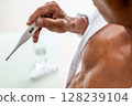 Man holding a digital thermometer showing a high temperature, indicating fever and self-care at home. 128239104