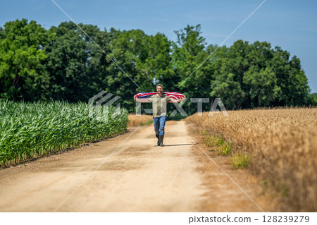 Man with American flag in crop field. Independence day of America. 4th of July. American Flag for labor Day or 4th of July. American flag and man farmer. Flag of the USA. Independence day Man with American flag in crop field. Independence day of America. 4th of July. American Flag for labor Day or 4th of July. American flag and man farmer. Flag of the USA. Independence day 128239279