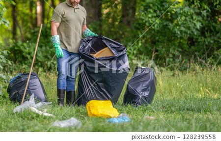 Man collecting plastic trash. Eco volunteer, cropped view. Garbage collecting in forest. Ecology concept. Volunteer collecting garbage, ecology. Man in rubber gloves with trash bag clean up garbage 128239558