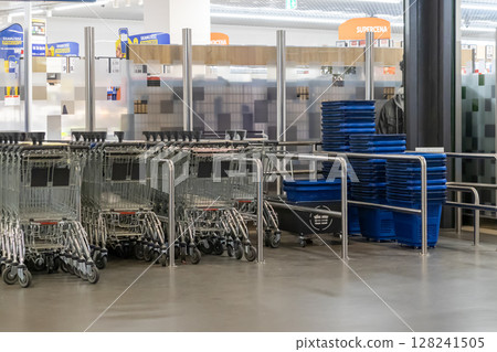 Neatly lined empty metal shopping carts and blue plastic baskets are ready for customer use within a modern, bright supermarket retail environment 128241505