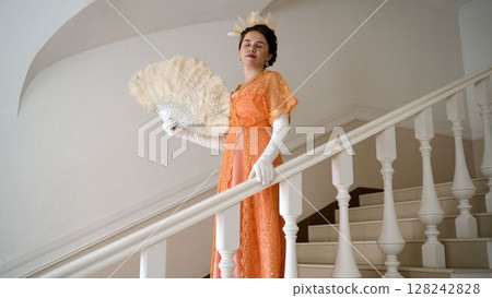 Elegant woman cooling herself with a feather fan on stairs 128242828