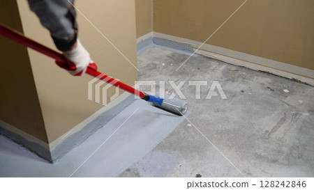 Applying an anti-slip layer to the floor of an underground parking lot. Paint the floor using a roller with a long handle. Painting the floor with a roller, repairing the floor. 128242846