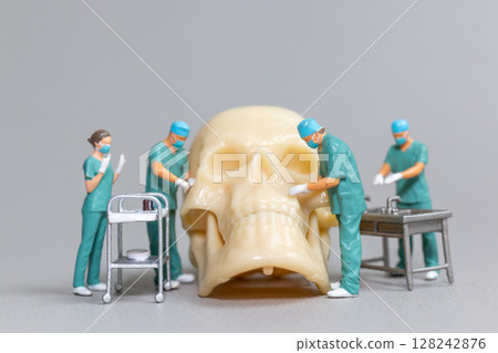 Miniature Surgeons Operating on Human Skull Model 128242876