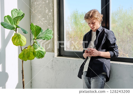 Serious teenage guy looking at smartphone screen, at home near window 128243200