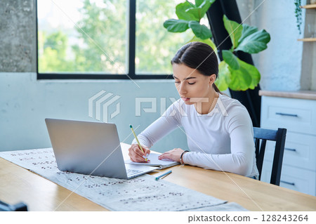 Teenage girl student sitting at the table with laptop, textbooks in home interior 128243264