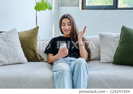 Young woman sitting at home on couch using smartphone Young woman sitting at home on couch using smartphone 128243304