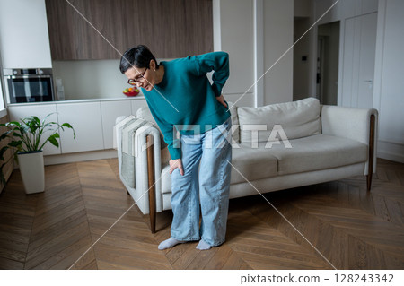 Middle aged woman bending in pain due to back injury. Lower back discomfort, spinal muscle strain 128243342