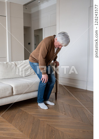 Old man suffering with knee joint pain. Elderly male howls struggling to rise from couch, arthrosis 128243577