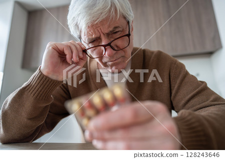 Pill blister check. Elderly man holds medication blister pack reading instructions with focused look Pill blister check. Elderly man holds medication blister pack reading instructions with focused look 128243646