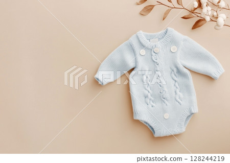 Baby knitted onesie on beige background. Fashion newborn clothes. Flat lay top view. Wool kid soft clothing. Infant trendy bodysuit made of organic eco friendly cotton. Children wardrobe. Baby garment 128244219