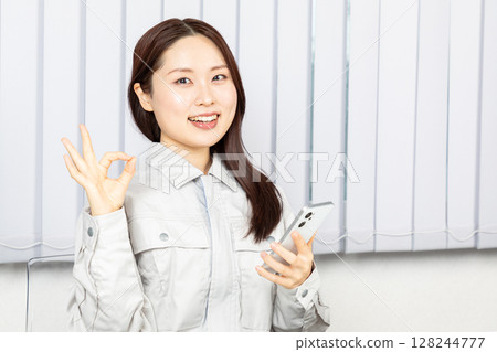Female worker holding a smartphone and giving an OK sign 01 128244777