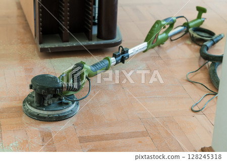 Wood Floor Sanding Process with Green Power Sander and Vacuum. Dust Removal Renovation, Interior Home Improvement, Bright Room, Close-up View 128245318