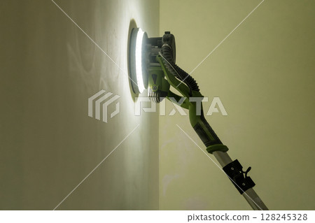 Wall Sanding with Telescopic Pole Sander: Close-Up of Green Power Tool Smoothing Interior Wall Surface, Bright Lighting, DIY Home Renovation Wall Sanding with Telescopic Pole Sander: Close-Up of Green Power Tool Smoothing Interior Wall Surface, Bright Lighting, DIY Home Renovation 128245328